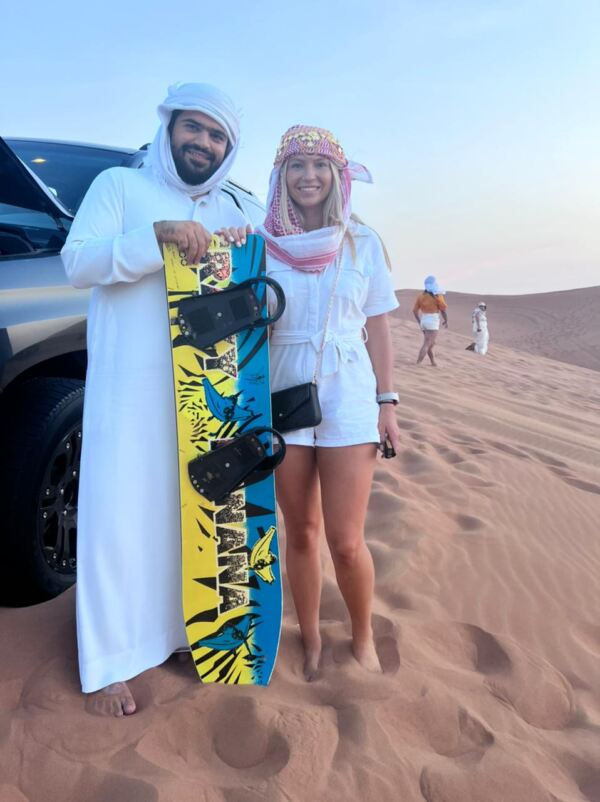 safari guide with a tourist carrying a sand board over desert safari tour